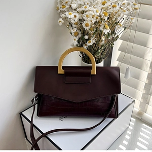 Detail of burgundy crocodile-embossed leather handbag with elegant handle and shoulder strap