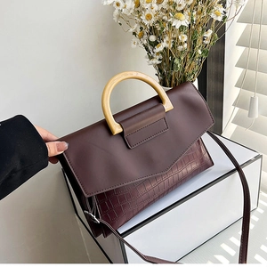 Detail of dark brown faux crocodile handbag featuring a wooden handle and leather strap