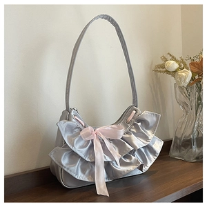 Detail of silver shoulder bag with mesh ruffles and a pink satin bow on a wooden surface