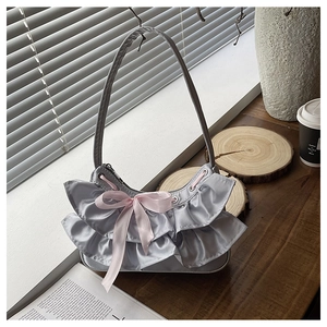 Detail of silver satin handbag featuring layered ruffles and a pink bow decoration