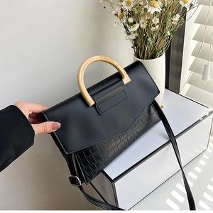 Detail of black faux crocodile clutch with stylish wood-grain handle and shadow lighting