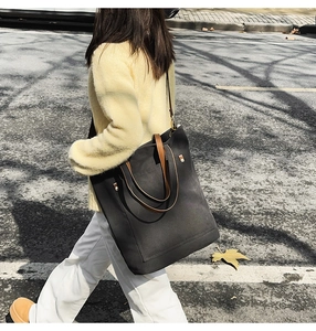 Detail of a large black canvas tote bag with brown leather handles for daily commuting