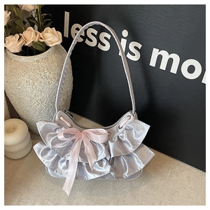 Close-up detail of silver satin underarm bag featuring pink bow and ruffle trim textures