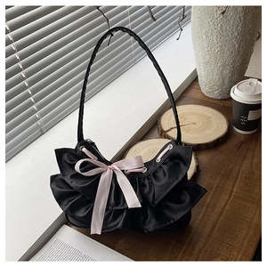 Detail of a black satin shoulder bag with ruffled edges and a pink silk ribbon bow