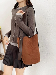 Minimalist brown suede bucket tote bag with adjustable leather strap worn by a model