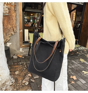 Detail of black canvas tote bag with brown leather handles and large capacity pocket