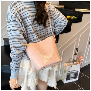 Detail of pink crocodile embossed bucket bag with metal feet and long shoulder strap