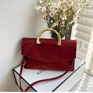 Detail of dark red crocodile pattern handbag with golden metal handle and fine texture