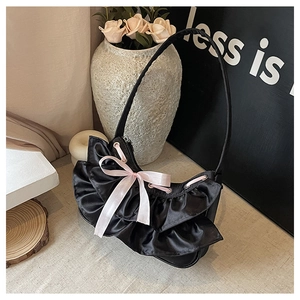 Close-up of black balletcore shoulder bag with ruffled edges and a pink satin bow detail