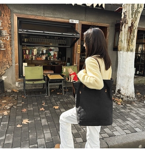 Street style view of a large black canvas tote bag with metal rivet reinforced pocket
