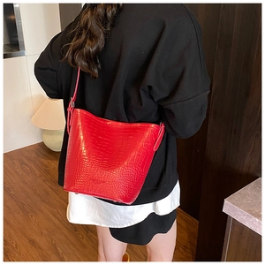 Close-up of red crocodile-patterned bucket bag with polished metal bottom studs