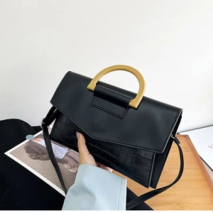 Detail of black faux leather clutch with crocodile texture and golden D-shaped handle