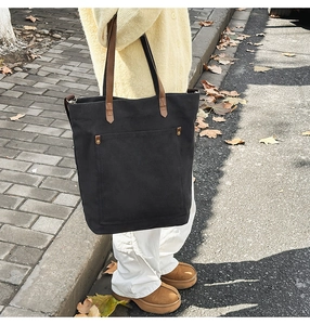 Detail of a large black canvas tote bag with leather straps on a street model