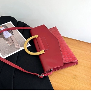Detail of red crocodile pattern clutch bag featuring elegant gold D-shaped handle