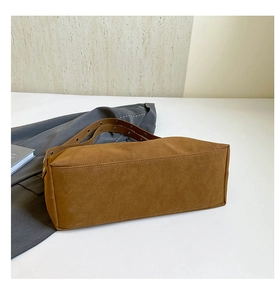 Detailed macro view of brown suede tote bag featuring reinforced metal rivet handles