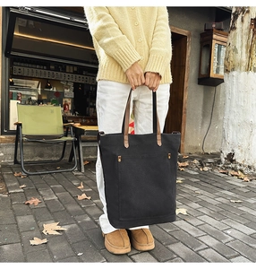 Outdoor shot of a black canvas tote bag with brown leather straps and front pocket detail