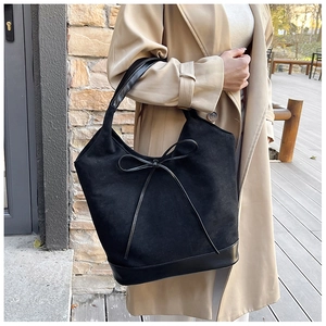 Détail du grand sac cabas en daim noir avec nœud en cuir porté par un mannequin à l'épaule