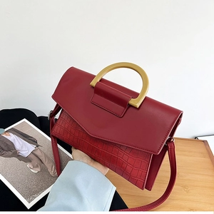 Detail of red faux leather handbag with crocodile texture and gold D-shaped metal handle