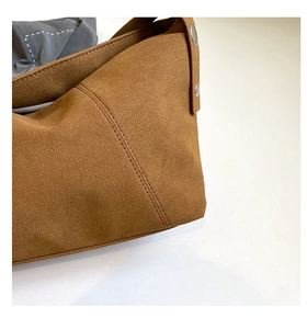 Detailed close-up of brown suede crossbody bag with double stitching and silver buckles