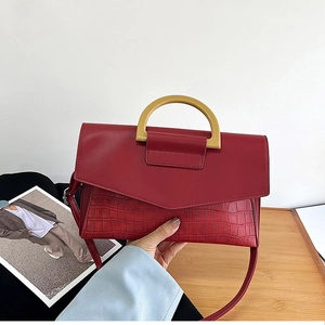 Detail view of burgundy crocodile texture handbag with D-shaped metal handle and strap