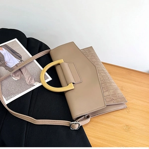 Detailed view of beige crocodile embossed leather handbag with D-shaped resin handle