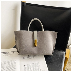 Detailed view of grey suede tote bag with golden metal buckle on leather chair