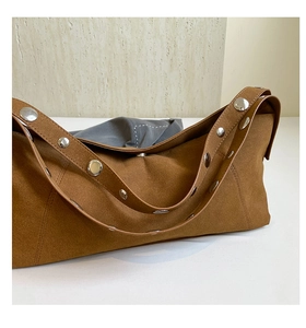 Detail shot of brown suede hobo bag featuring silver metal rivets on the wide strap