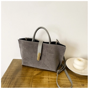 Detailed close-up of grey frosted suede tote bag featuring a gold metal buckle on a desk