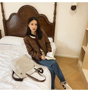 Lifestyle shot of a large beige canvas tote bag with dark brown straps on a white bed