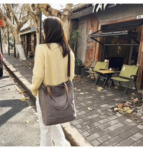 Outdoor street view of a large dark brown canvas tote bag with leather strap accents