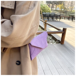 Detail of purple frosted suede mini envelope bag with gold chain strap on trench coat