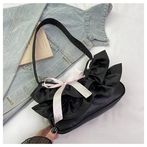 Detail of elegant black satin handbag with layered ruffles and soft pink silk bow