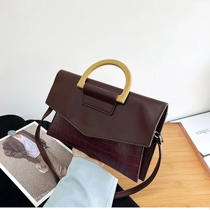 Detail of dark brown faux crocodile leather bag with amber resin handle and flap closure