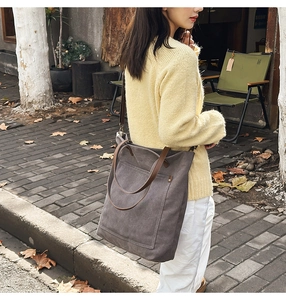 Outdoor street view of a large vintage dark grey canvas tote bag with brown leather handles