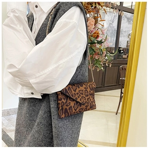 Detail shot of leopard print envelope bag featuring a gold chain strap on a model