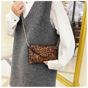Detail view of leopard print envelope clutch with gold chain strap on model outfit