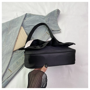 Detailed top view of black satin handbag with ruffled trim on white fabric background
