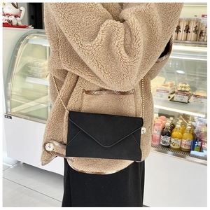 Detail of a black matte envelope crossbody bag with fine stitching and golden chain strap