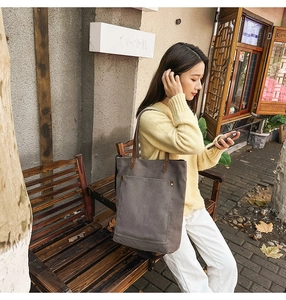 Detail of vintage canvas tote bag with front pocket and leather straps in street setting