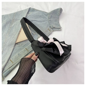 Detail of black satin shoulder bag featuring ruffled lace edges and pink ribbon accent