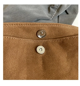 Close-up of brown suede crossbody bag featuring silver magnetic clasp and contrast stitching
