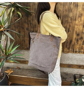 Detail of grey canvas tote bag with brown leather handles and metal rivet reinforcement