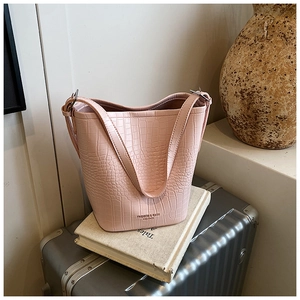 Detail shot of a pink crocodile pattern bucket bag on a vintage book and suitcase