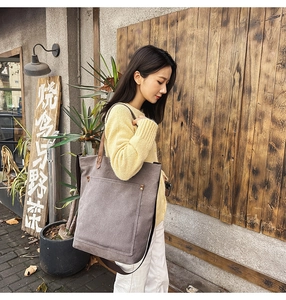 Detail of taupe canvas tote bag featuring brown leather handles and metal rivet reinforcement