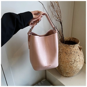 Detail view of light pink crocodile pattern bucket bag with leather strap and metal buckle