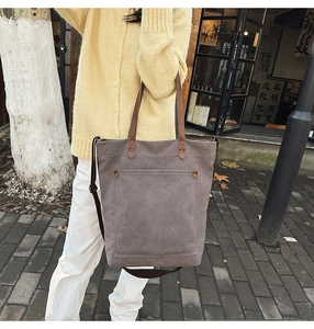 Detail of dark gray canvas tote bag with brown leather handles and metal rivet accents