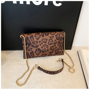 Detail of leopard print envelope bag with golden chain strap on a textured surface