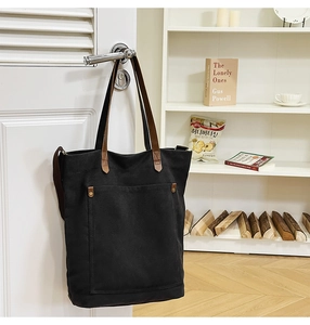 Detail of a black canvas tote bag with brown straps hanging on a white door handle
