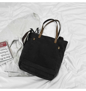 Detail of black canvas tote bag showing metal rivets on the pocket and sturdy brown straps