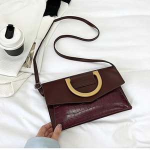 Detail of burgundy crocodile-embossed clutch bag featuring a golden decorative clasp